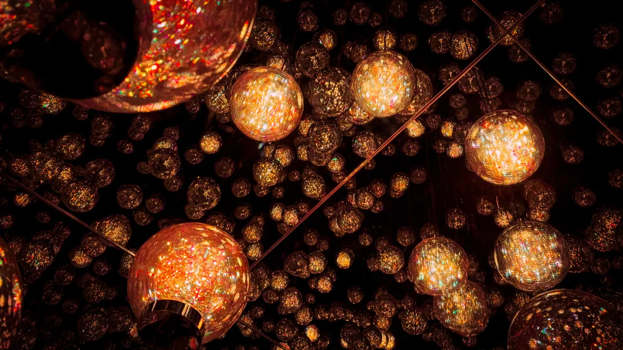 Hundreds of amber glass spheres hanging in the dark, a few close and glowing, the rest receding into points of light.