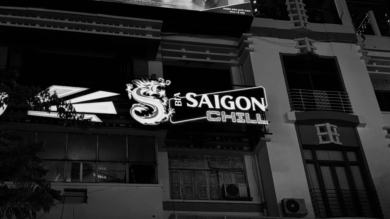 Black and white: a neon sign reading Bia Saigon Chill, with a coiled dragon, on the front of an old building at night.