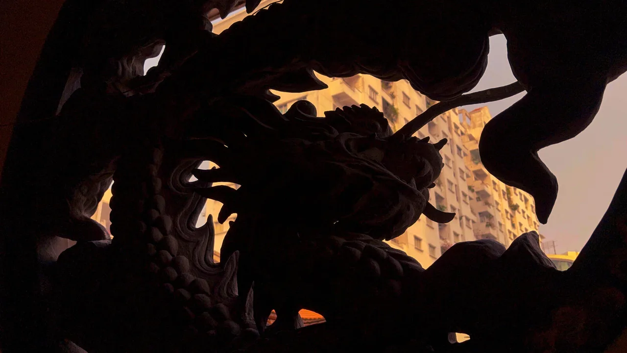 A carved dragon in silhouette, and through its curves an apartment tower lit orange by the evening sun.