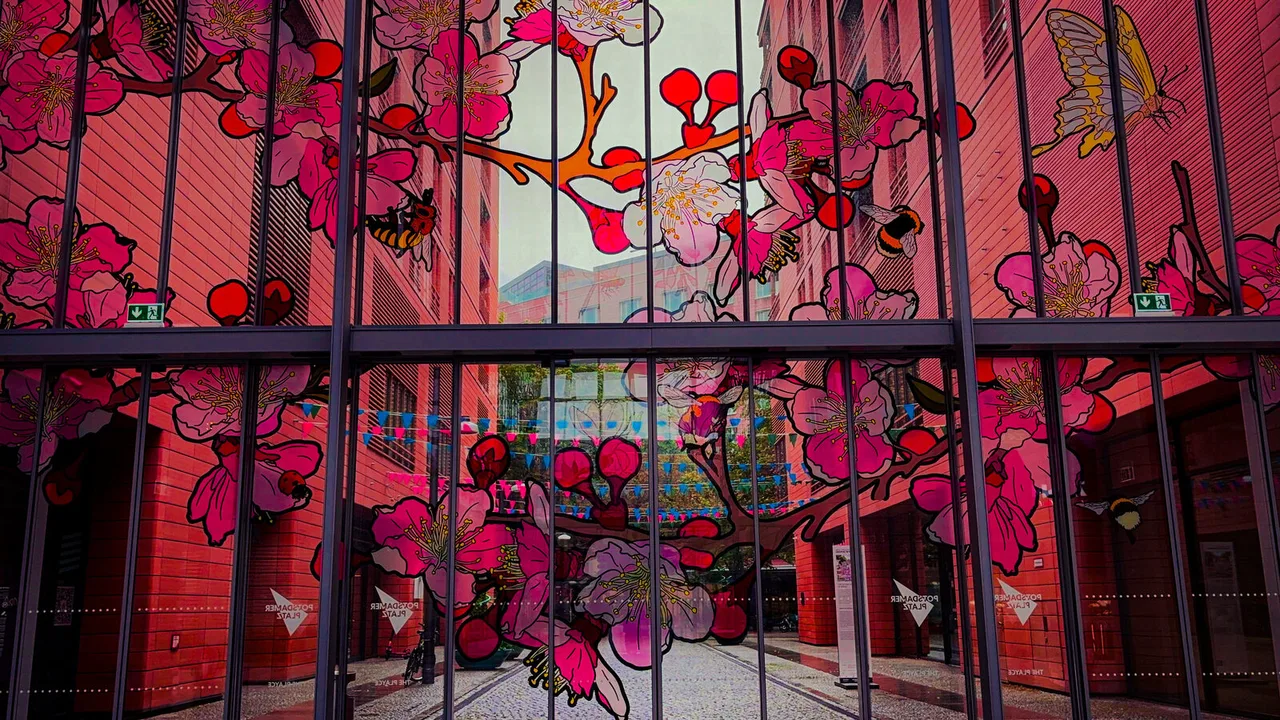 A glass wall painted with pink cherry blossoms, bees and a butterfly, looking through to a passage of red brick.